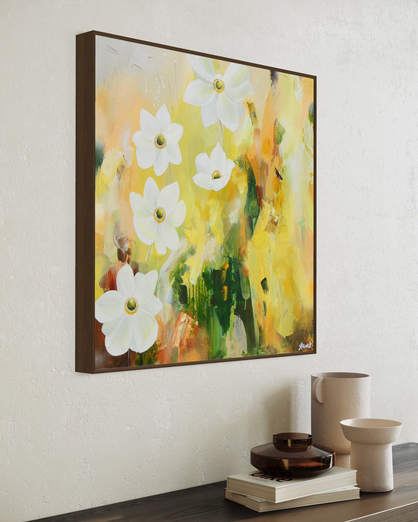 A 'Fresh Start' original acrylic painting by Jasmine Marshall framed in black/oak. Canvas painting features white anemone flowers atop cream, lime green, yellow, and brown abstract details, featured in a neutral home interior on a bookshelf..