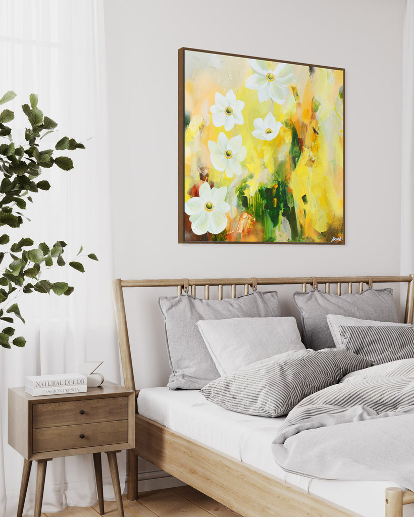 A 'Fresh Start' original acrylic painting by Jasmine Marshall framed in black/oak. Canvas painting features white anemone flowers atop cream, lime green, yellow, and brown abstract details, featured in a neutral home interior with a white bed and wooden bedside table.