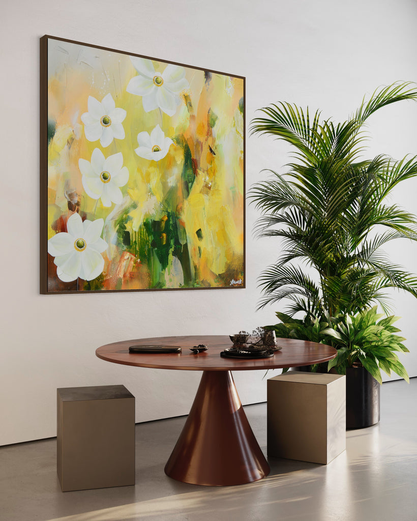 A 'Fresh Start' original acrylic painting by Jasmine Marshall framed in black/oak. Canvas painting features white anemone flowers atop cream, lime green, yellow, and brown abstract details, featured in a neutral home interior with a plant and wooden dining table..