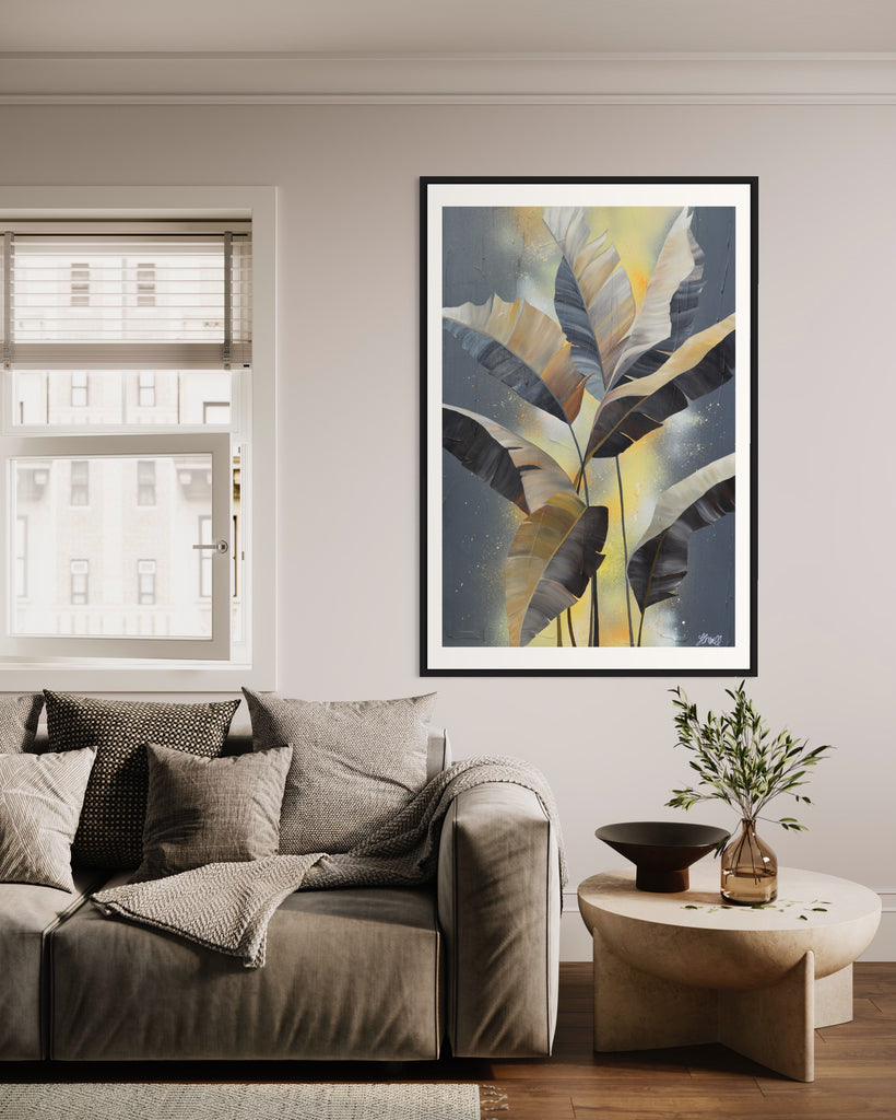 'Bittersweet' Fine Art Print by Jasmine Marshall, framed in black/oak. Premium Giclée print features grey palm leaves on an abstract yellow background. Featured in a neutral home living room with grey sofa and wooden coffee table.