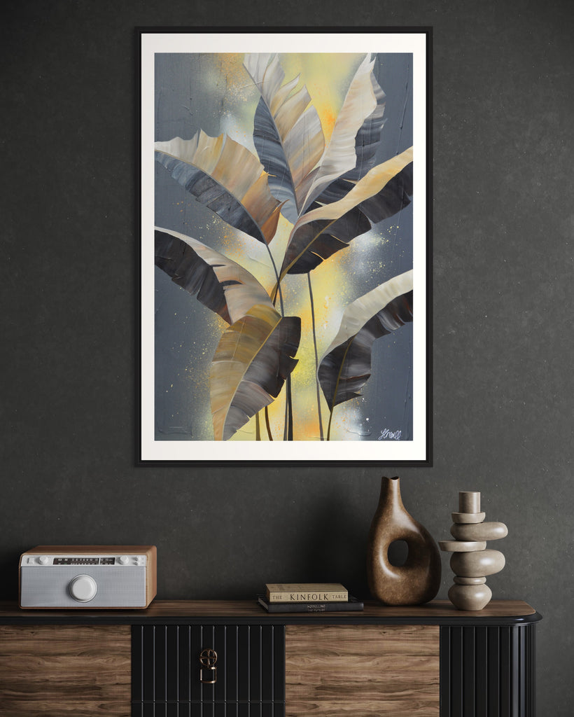 'Bittersweet' Fine Art Print by Jasmine Marshall, framed in black/oak. Premium Giclée print features grey palm leaves on an abstract yellow background. Featured on a dark grey wall and wooden unit.