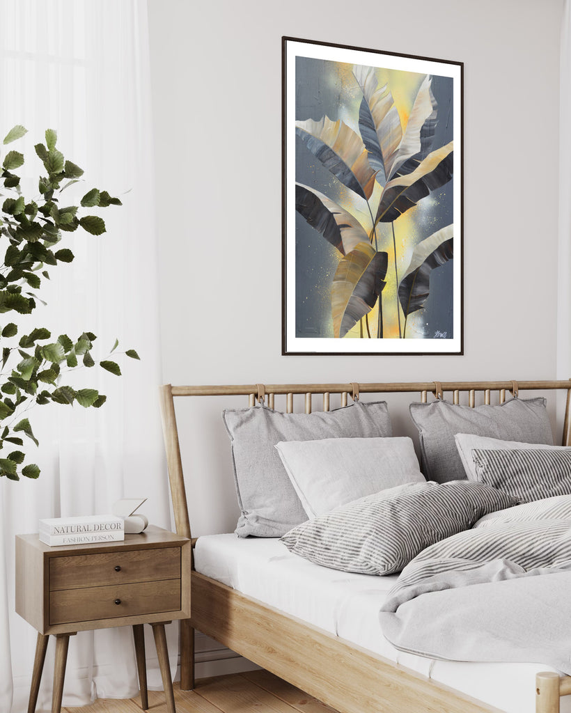 'Bittersweet' Fine Art Print by Jasmine Marshall, framed in black/oak. Premium Giclée print features grey palm leaves on an abstract yellow background. Featured in a neutral home interior with white bed and wooden bedside table.