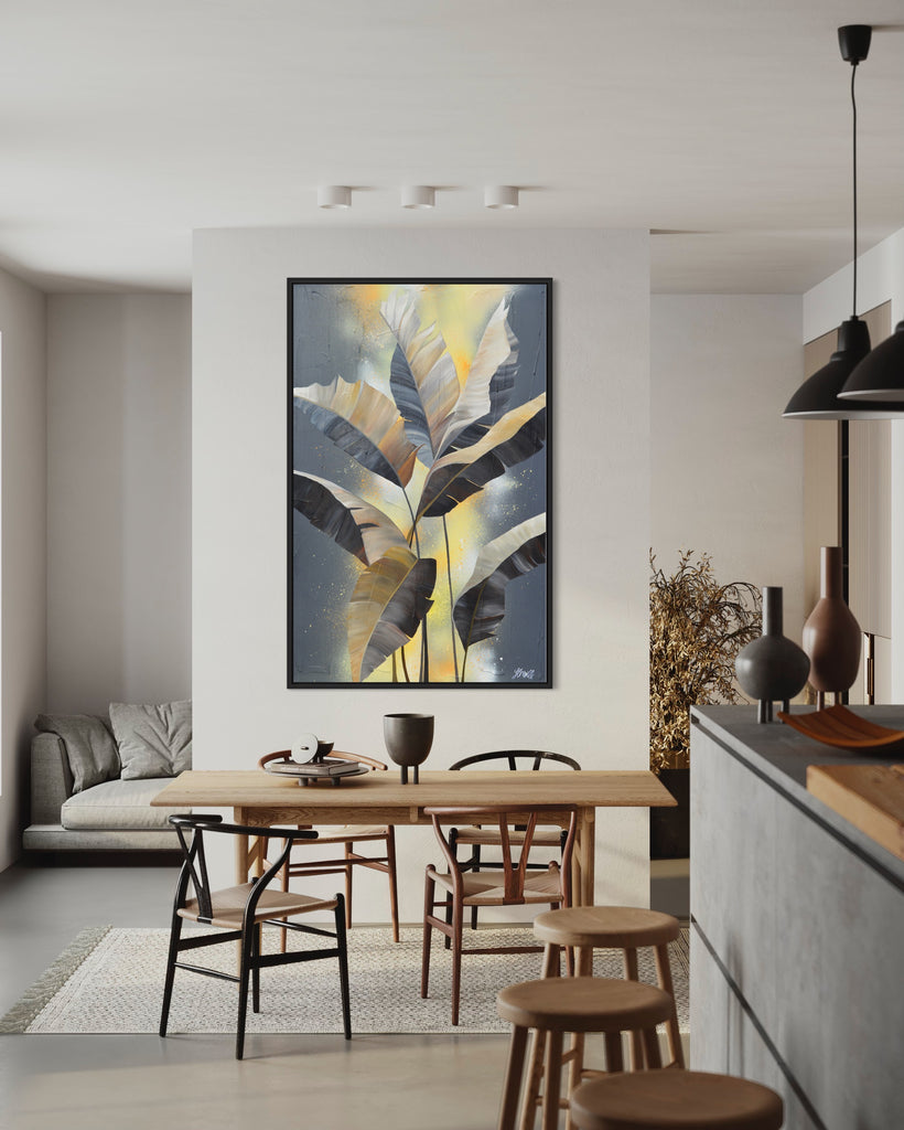 'Bittersweet' original acrylic painting by Jasmine Marshall framed in black/oak. Canvas painting features grey palm leaves on an abstract yellow background. Featured in a neutral kitchen with a wooden dining table..