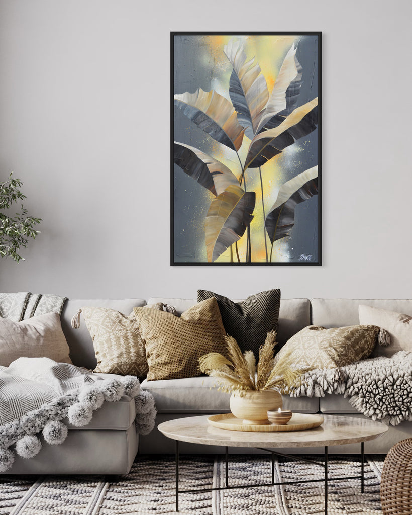 'Bittersweet' original acrylic painting by Jasmine Marshall framed in black/oak. Canvas painting features grey palm leaves on an abstract yellow background. Featured in a neutral home interior with a grey sofa and yellow cushions.