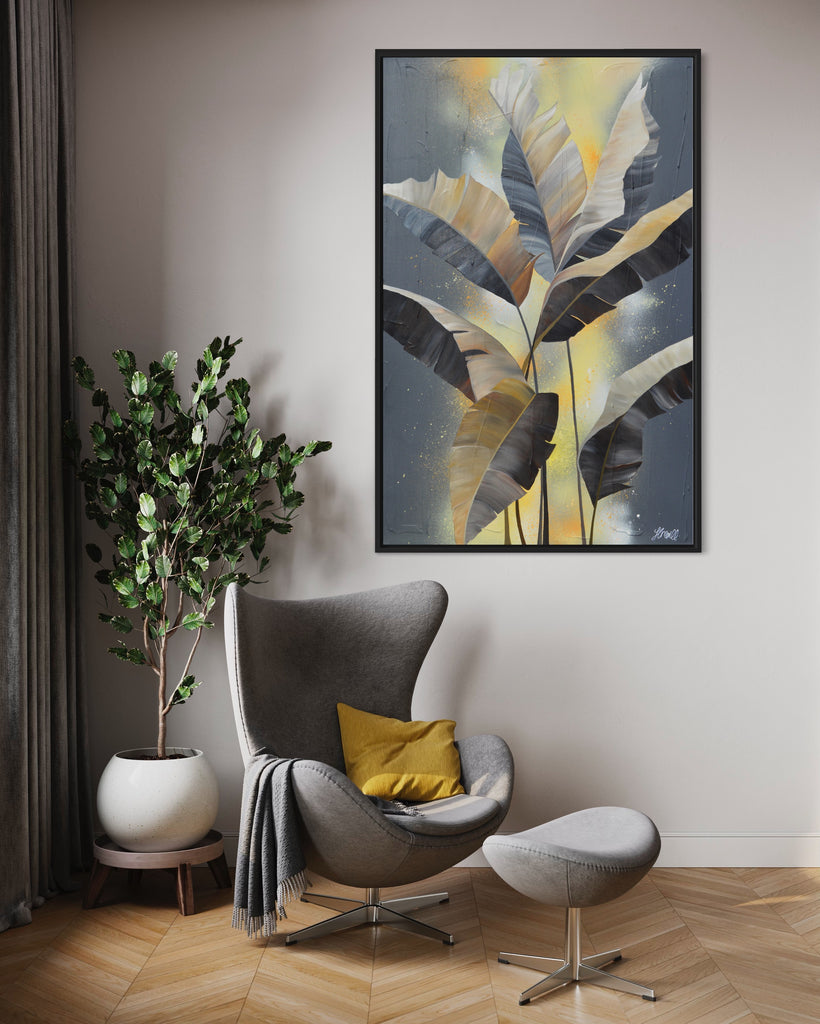 'Bittersweet' original acrylic painting by Jasmine Marshall framed in black/oak. Canvas painting features grey palm leaves on an abstract yellow background. Featured in a neutral home interior with a grey chair, yellow cushions, grey curtains and a plant.s.