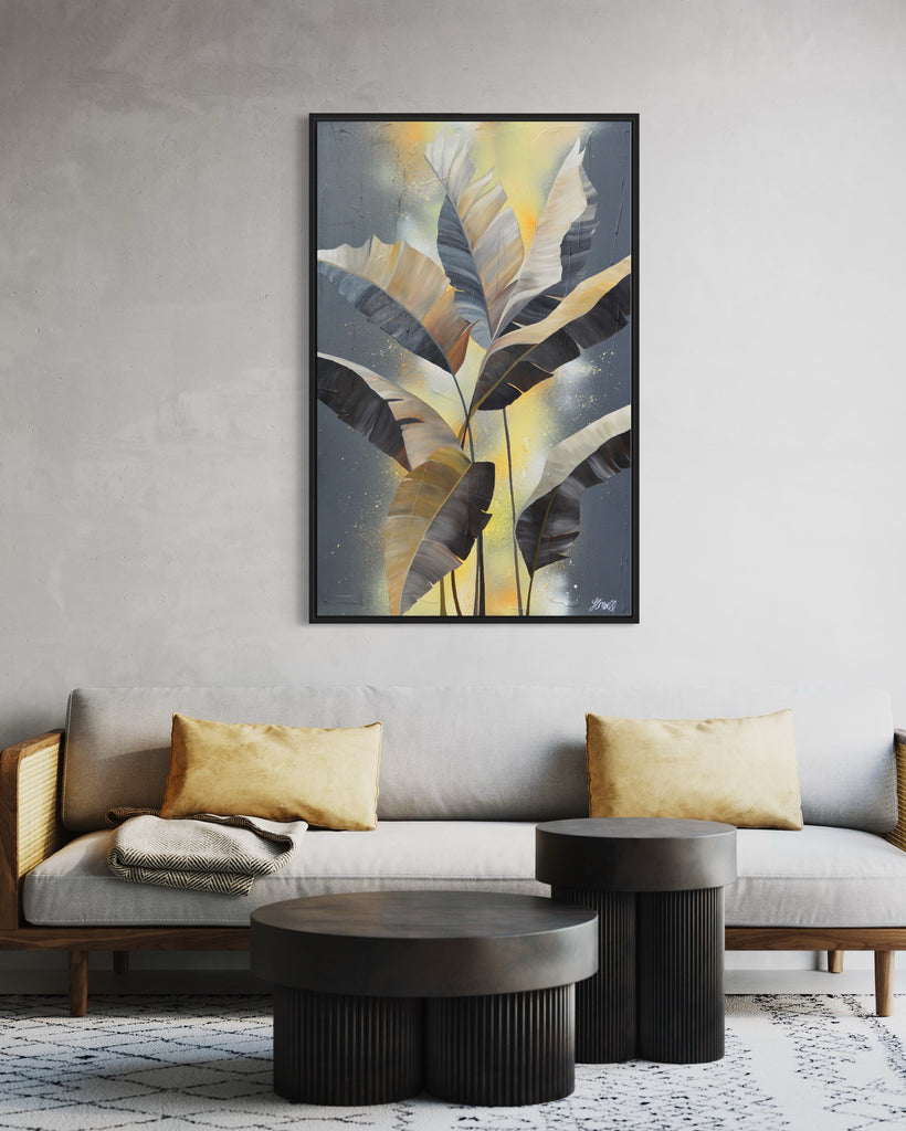 'Bittersweet' original acrylic painting by Jasmine Marshall framed in black/oak. Canvas painting features grey palm leaves on an abstract yellow background. Featured in a neutral home interior with a grey sofa and yellow cushions.