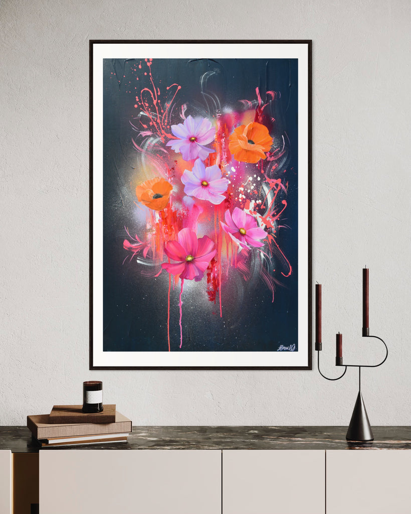 A 'Drama Tropicana' Fine Art Print by Jasmine Marshall, framed in black/oak. Premium Giclée print features white orange poppies and pink and purple flower on an abstract navy background, featured in a neutral home interior with candles and books.