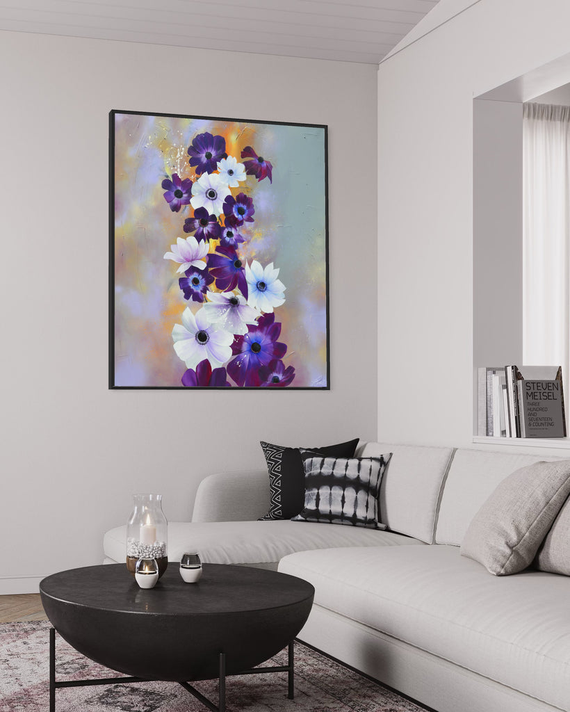 'Flourish' original painting on a cotton canvas by Jasmine Marshall, framed in black/oak. Features white and purple anemone flowers on a grey and lilac abstract background, featured in a neutral home interior with white sofa and black coffee table.