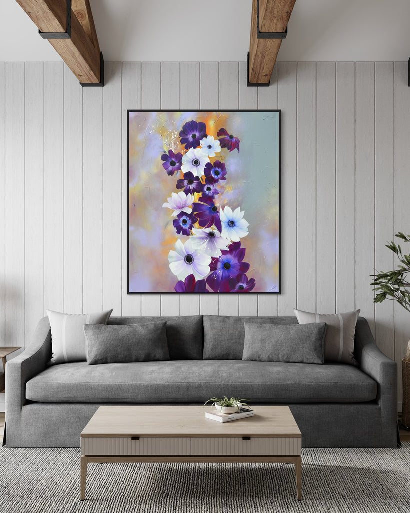 'Flourish' original painting on a cotton canvas by Jasmine Marshall, framed in black/oak. Features white and purple anemone flowers on a grey and lilac abstract background, featured in a neutral home interior. with wooden ceiling beams, grey sofa, tree and coffee table.