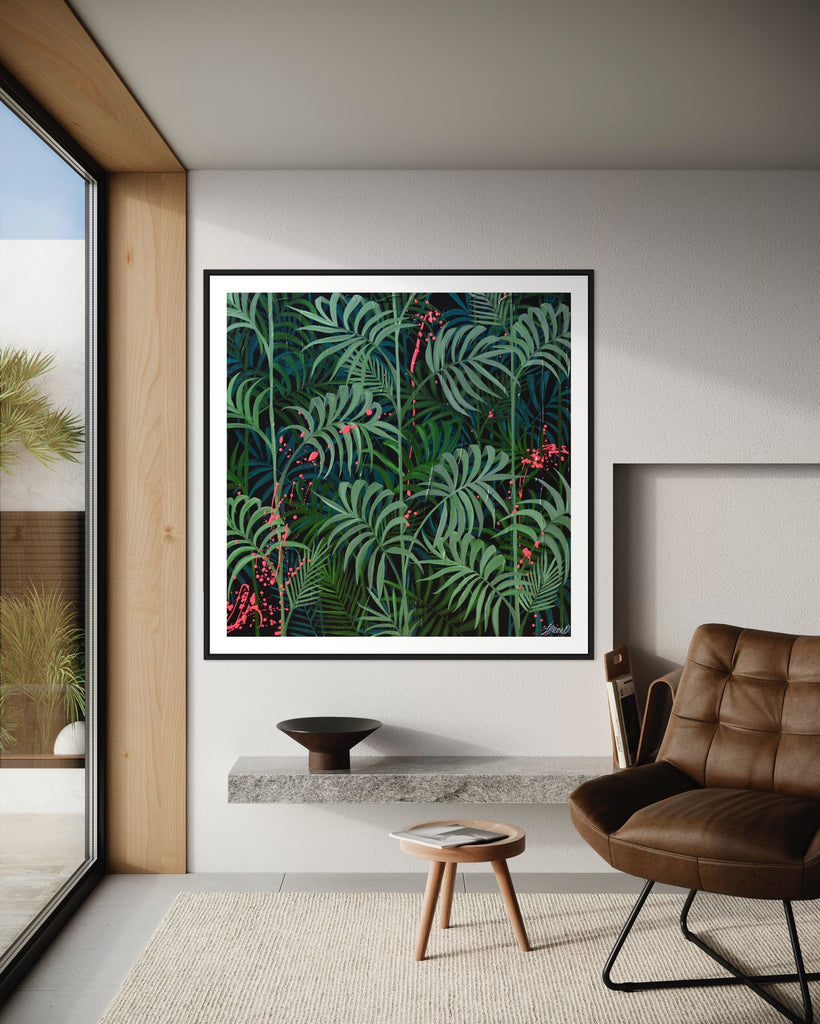 ‘Forever Green' Fine Art Print by Jasmine Marshall, framed in black/oak. Premium Giclée print features layers of palm leaves on a black background with pops on neon pink.  Displayed in a neutral home interior, with brown chair and window overlooking the garden.