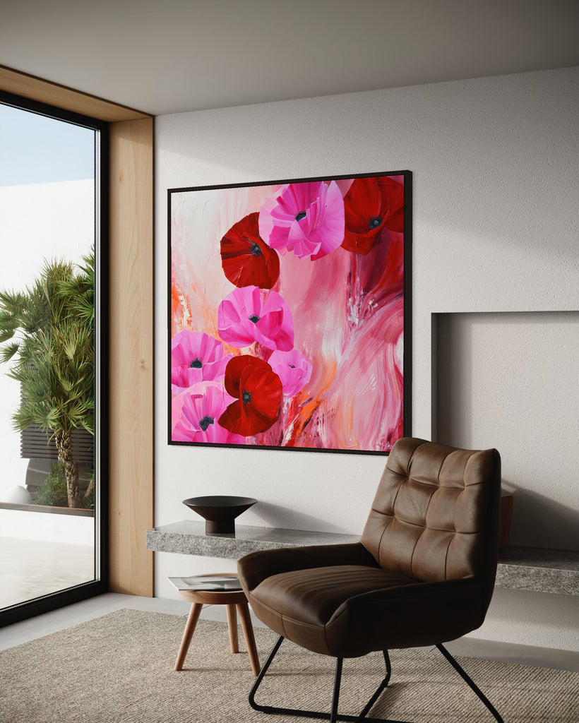 'It’s a Forever Thing' original painting on a cotton canvas by Jasmine Marshall, framed in black/oak. Features pink and red poppies on an abstract background with pops of orange. Displayed on a white wall next to a brown chair overlooking a garden..