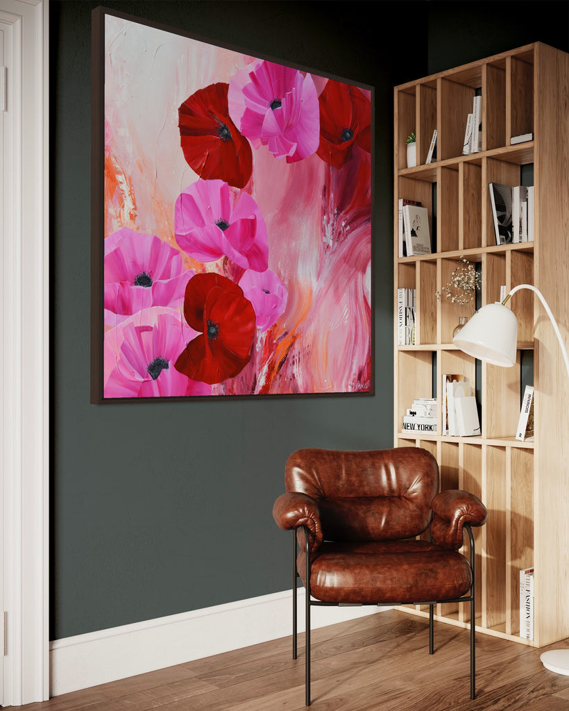 'It’s a Forever Thing' original painting on a cotton canvas by Jasmine Marshall, framed in black/oak. Features pink and red poppies on an abstract background with pops of orange. Displayed on a green wall with wooden bookshelf, brown leather chair and lamp.