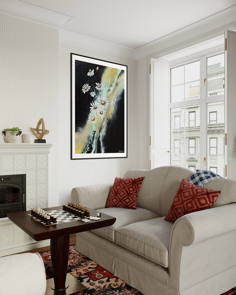 ‘Light in the Darkness' Fine Art Print by Jasmine Marshall, framed in black/oak. Premium Giclée print features white daisies on a black abstract background.  Displayed in a neutral home interior with white sofas, chess board and red cushions overlooking the city.