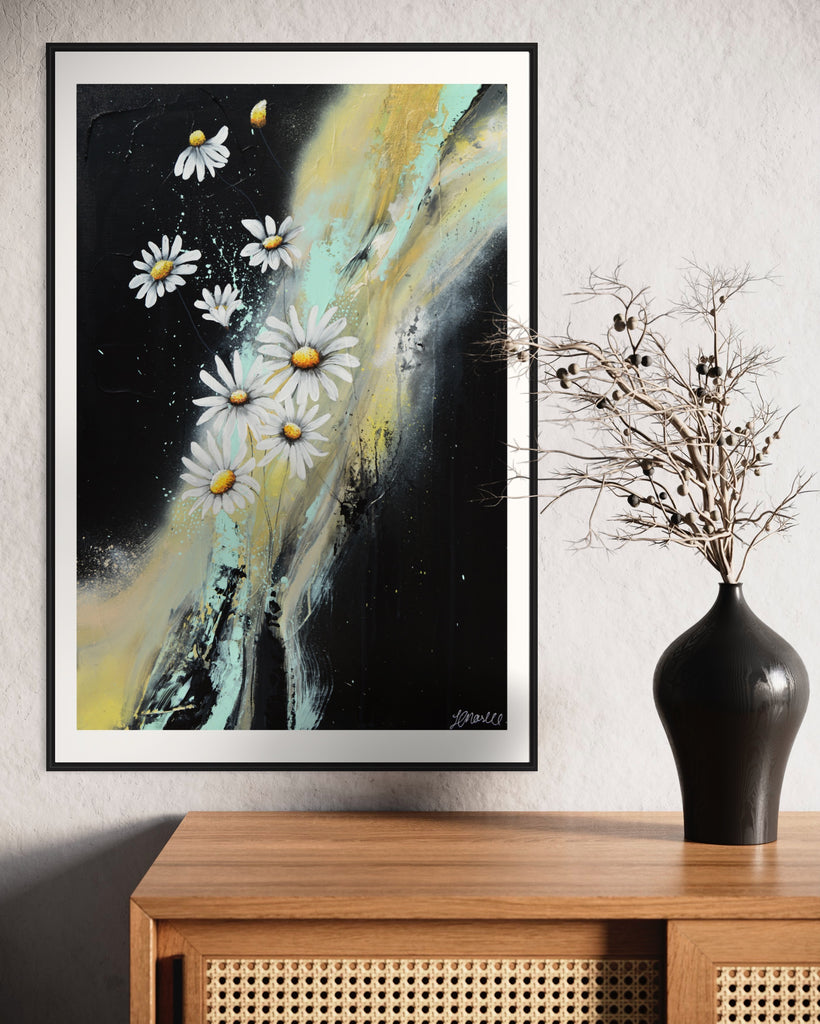 ‘Light in the Darkness' Fine Art Print by Jasmine Marshall, framed in black/oak. Premium Giclée print features white daisies on a black abstract background.  Displayed in a neutral home interior with wooden wide table and black vase.