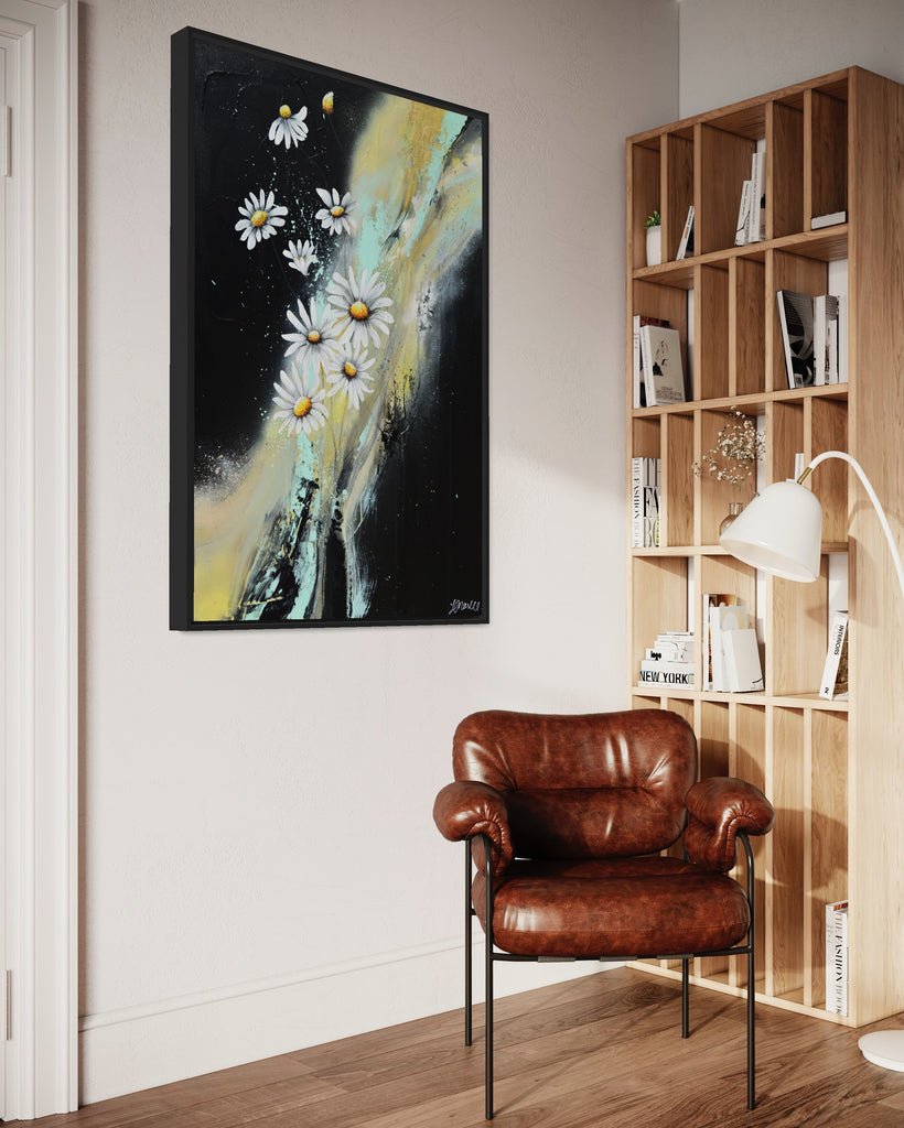 'Light in the Darkness' original painting on a cotton canvas by Jasmine Marshall, framed in black/oak. Features white daisies on a black abstract background. Displayed in a neutral home interior with wooden book shelf and brown leather chair.