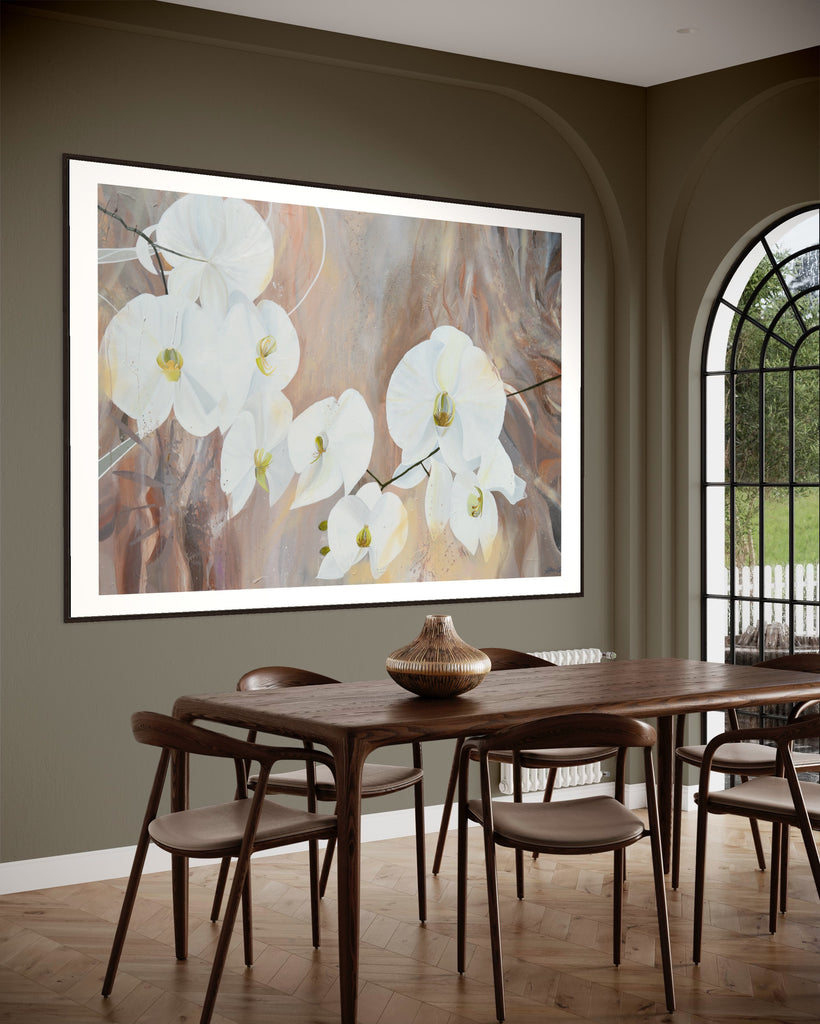 ‘Natural Elegance' Fine Art Print by Jasmine Marshall, framed in black/oak. Premium Giclée print features white orchids on a neutral brown, beige abstract background. Displayed in a kitchen with khaki walls, glass door and wooden dining table.