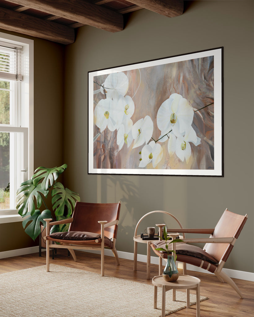 ‘Natural Elegance' Fine Art Print by Jasmine Marshall, framed in black/oak. Premium Giclée print features white orchids on a neutral brown, beige abstract background. Displayed in a neutral home interior with khaki walls, a plant, wooden ceiling beams and brown leather chairs.