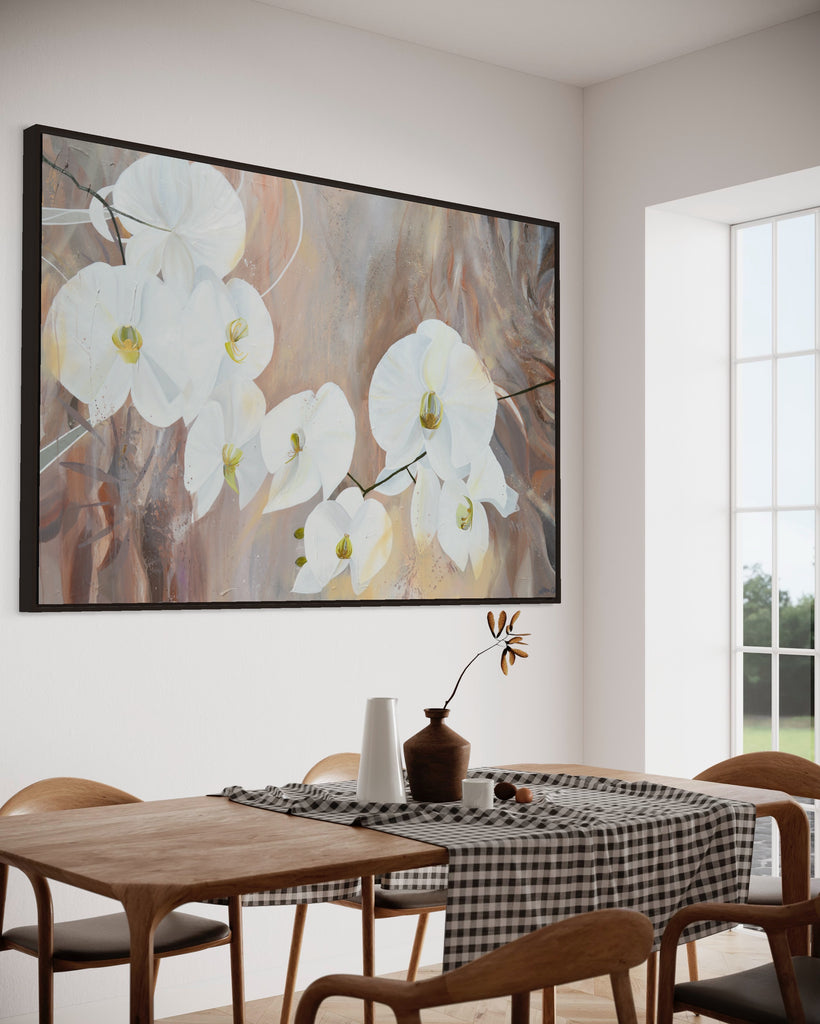 'Natural Elegance' original painting on a cotton canvas by Jasmine Marshall, framed in black/oak. Features white orchids on a neutral brown, beige abstract background. Displayed in a neutral home interior with a wooden dining table and big window.