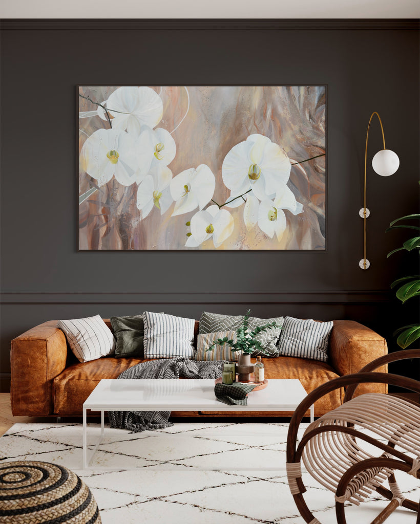 'Natural Elegance' original painting on a cotton canvas by Jasmine Marshall, framed in black/oak. Features white orchids on a neutral brown, beige abstract background. Displayed in a living room with dark grey walls, brown sofa, white rug and plant.