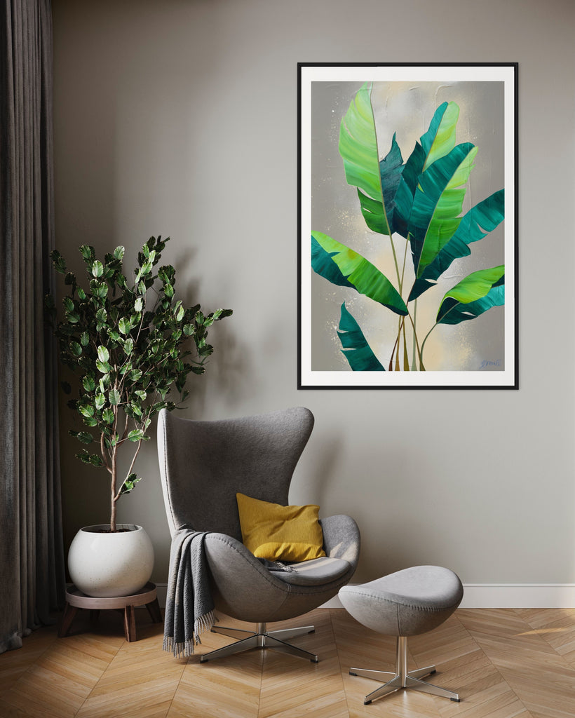 ‘Rainforest Glow' Fine Art Print by Jasmine Marshall, framed in black/oak. Premium Giclée print features green palm leaves on a neutral abstract painting. Displayed in a neutral home interior that has a grey chair, yellow cushion and plant in.