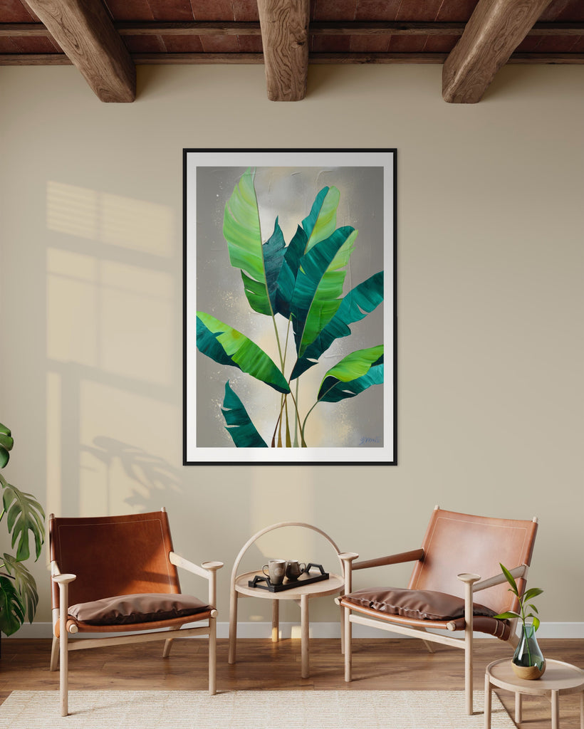 ‘Rainforest Glow' Fine Art Print by Jasmine Marshall, framed in black/oak. Premium Giclée print features green palm leaves on a neutral abstract painting. Displayed in a neutral home interior with brown wooden ceiling beams, brown chairs and plant.