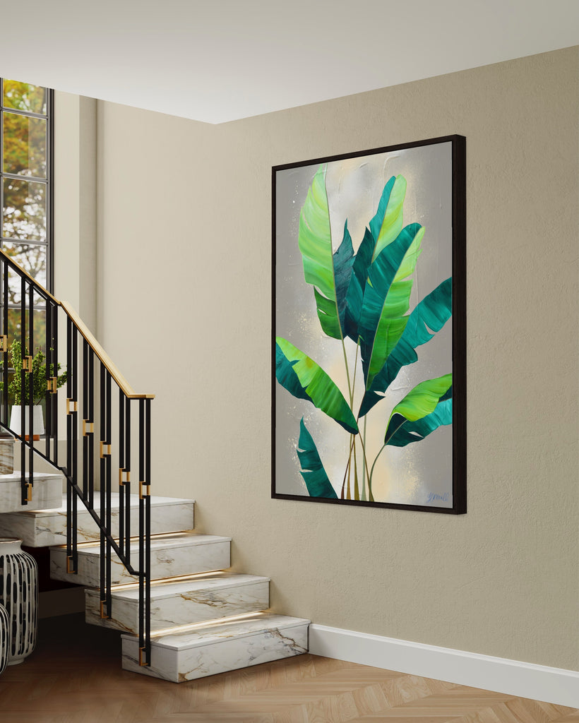 'Rainforest Glow' original painting on a cotton canvas by Jasmine Marshall, framed in black/oak. Features green palm leaves on a neutral abstract painting. Displayed in a neutral home interior next to a marble staircase.