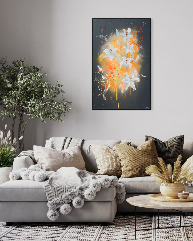 'Sweet Pollen' original painting on a cotton canvas by Jasmine Marshall, framed in black/oak. Features white lilies on a grey textured background with pops of neon orange. Displayed in a neutral home interior with grey sofa, yellow cushions, wooden coffee table and plant.