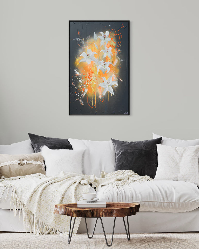 'Sweet Pollen' original painting on a cotton canvas by Jasmine Marshall, framed in black/oak. Features white lilies on a grey textured background with pops of neon orange. Displayed in a neutral living room with white sofas and grey cushions and a wooden coffee table.