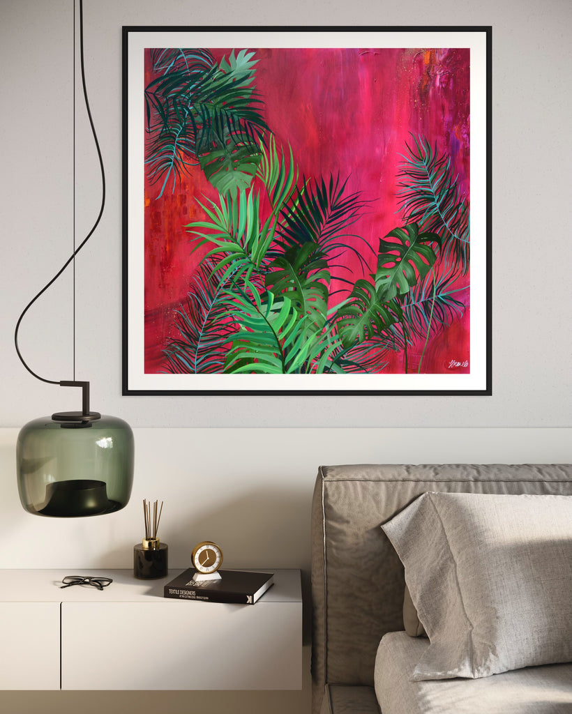 ‘The Foliage' Fine Art Print by Jasmine Marshall, framed in black/oak. Premium Giclée print features tropical leaves over an abstract pink, red and orange painting. Displayed in a neutral home interior above a grey bed with green glass light.