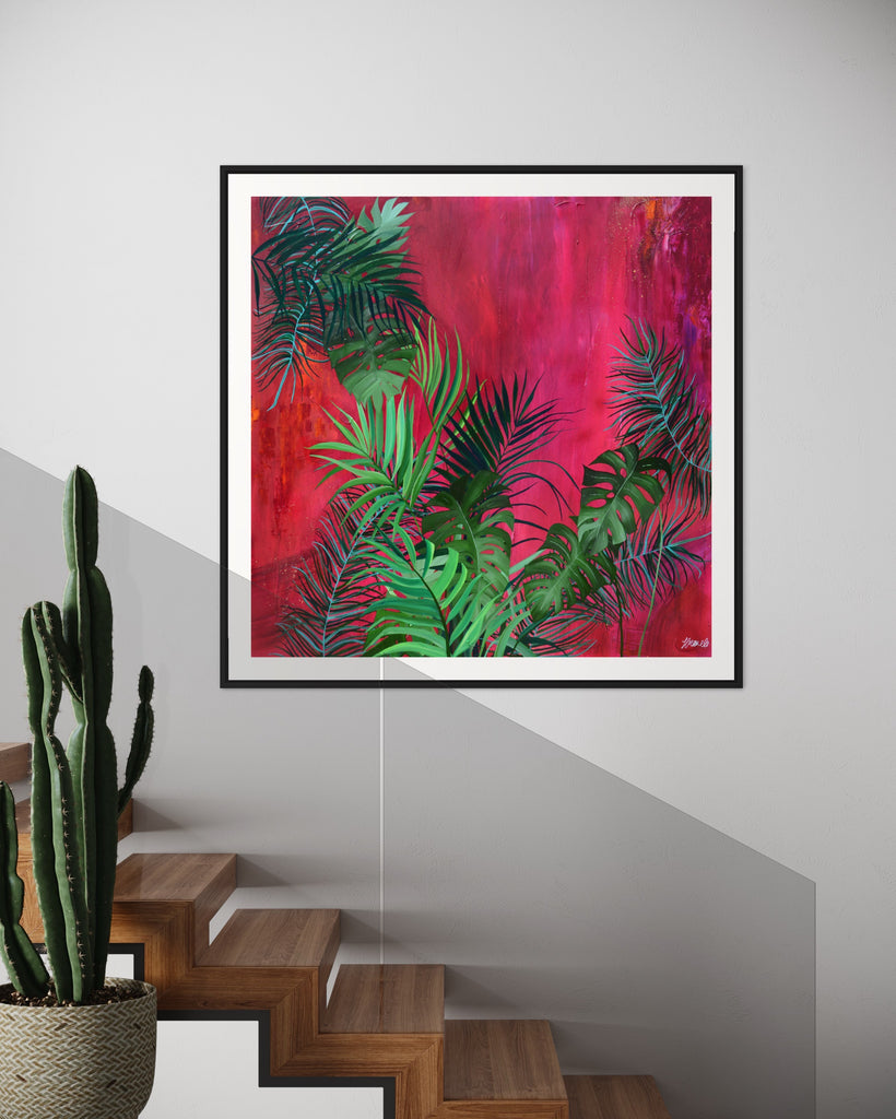 ‘The Foliage' Fine Art Print by Jasmine Marshall, framed in black/oak. Premium Giclée print features tropical leaves over an abstract pink, red and orange painting. Displayed in above a wooden staircase next to a cactus plant.