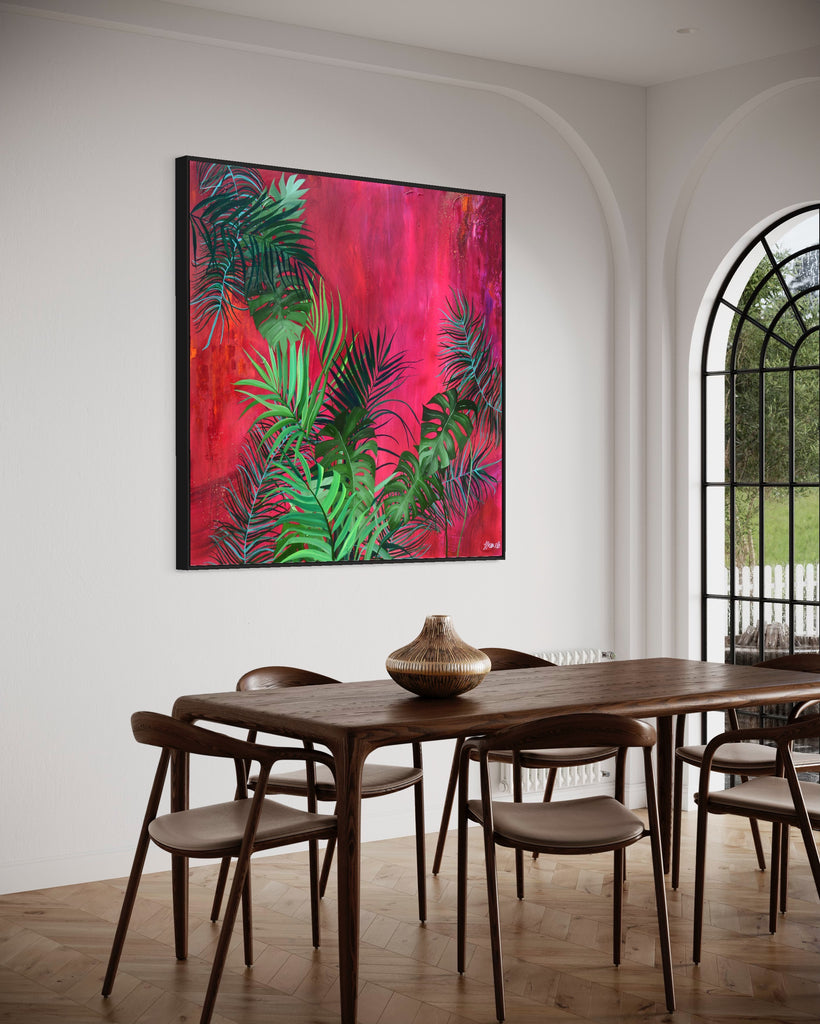 'The Foliage' original painting on a cotton canvas by Jasmine Marshall, framed in black/oak. Features tropical leaves over an abstract pink, red and orange painting Displayed in a neutral home interior with wooden dining table and glass doors.