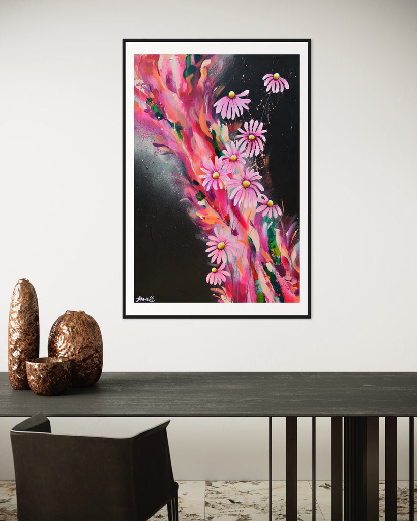 ‘The Laughter of Daisies' Fine Art Print by Jasmine Marshall, framed in black/oak. Premium Giclée print features pink daises on a colourful abstract details on a black background. Displayed in a neutral home interior.