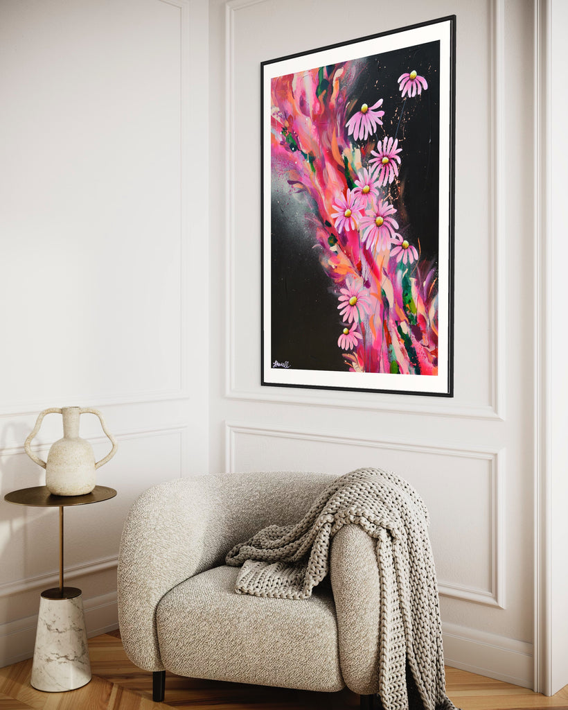 ‘The Laughter of Daisies' Fine Art Print by Jasmine Marshall, framed in black/oak. Premium Giclée print features pink daises on a colourful abstract details on a black background. Displayed in a neutral home interior with grey armchair and white wall paneling.