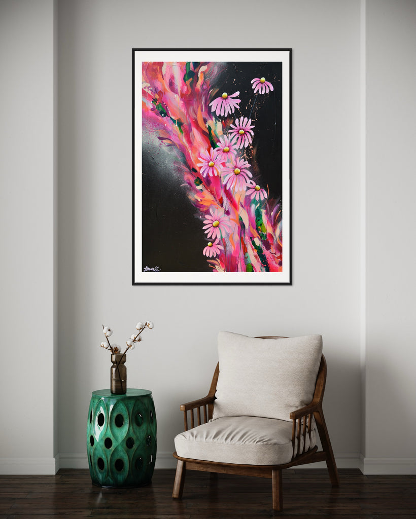 ‘The Laughter of Daisies' Fine Art Print by Jasmine Marshall, framed in black/oak. Premium Giclée print features pink daises on a colourful abstract details on a black background. Displayed in a neutral home interior with green table and brown chair.