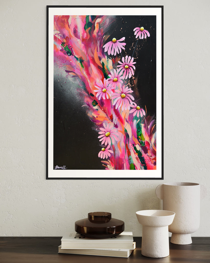 ‘The Laughter of Daisies' Fine Art Print by Jasmine Marshall, framed in black/oak. Premium Giclée print features pink daises on a colourful abstract details on a black background. Displayed in a neutral home interior on a wooden shelf with books.