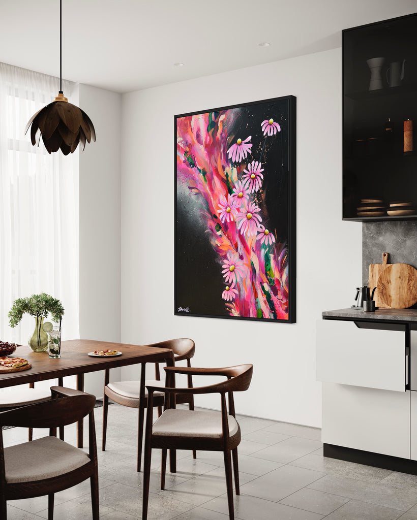 'The Laughter of Daisies' original painting on a cotton canvas by Jasmine Marshall, framed in black/oak. Features pink daises on a colourful abstract details on a black background. Displayed in a kitchen with wooden dining table.