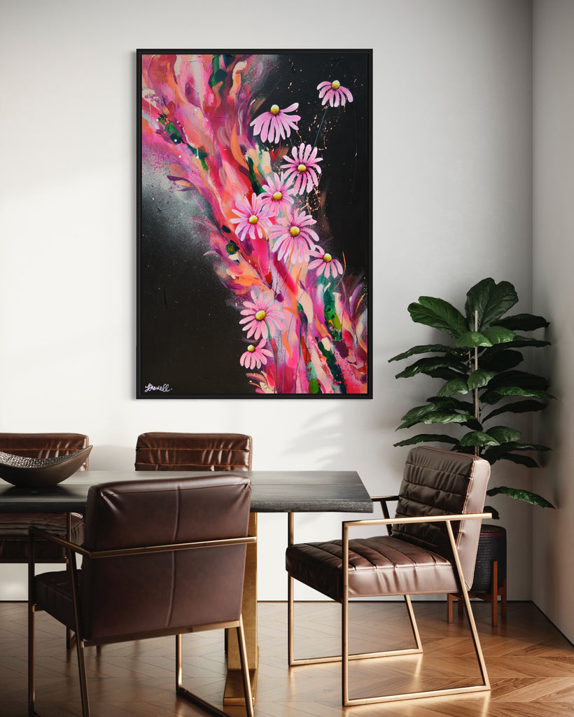 'The Laughter of Daisies' original painting on a cotton canvas by Jasmine Marshall, framed in black/oak. Features pink daises on a colourful abstract details on a black background. Displayed in a dining room with brown table and green plant.