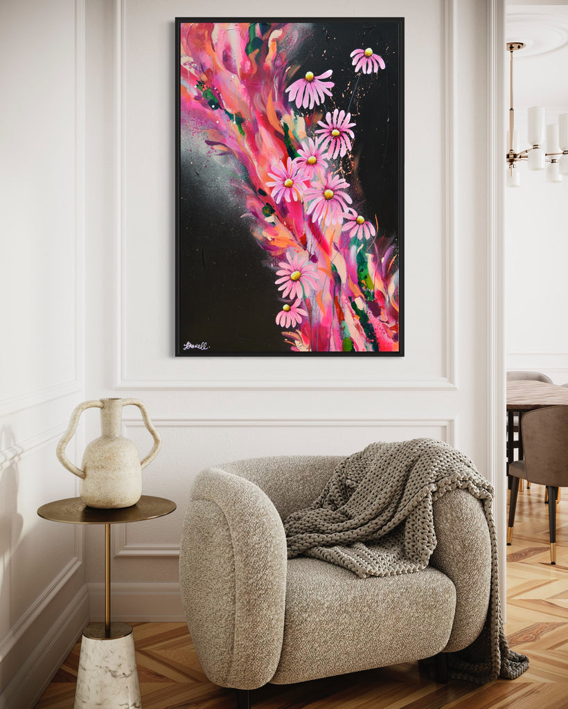 'The Laughter of Daisies' original painting on a cotton canvas by Jasmine Marshall, framed in black/oak. Features pink daises on a colourful abstract details on a black background. Displayed in a neutral home interior.