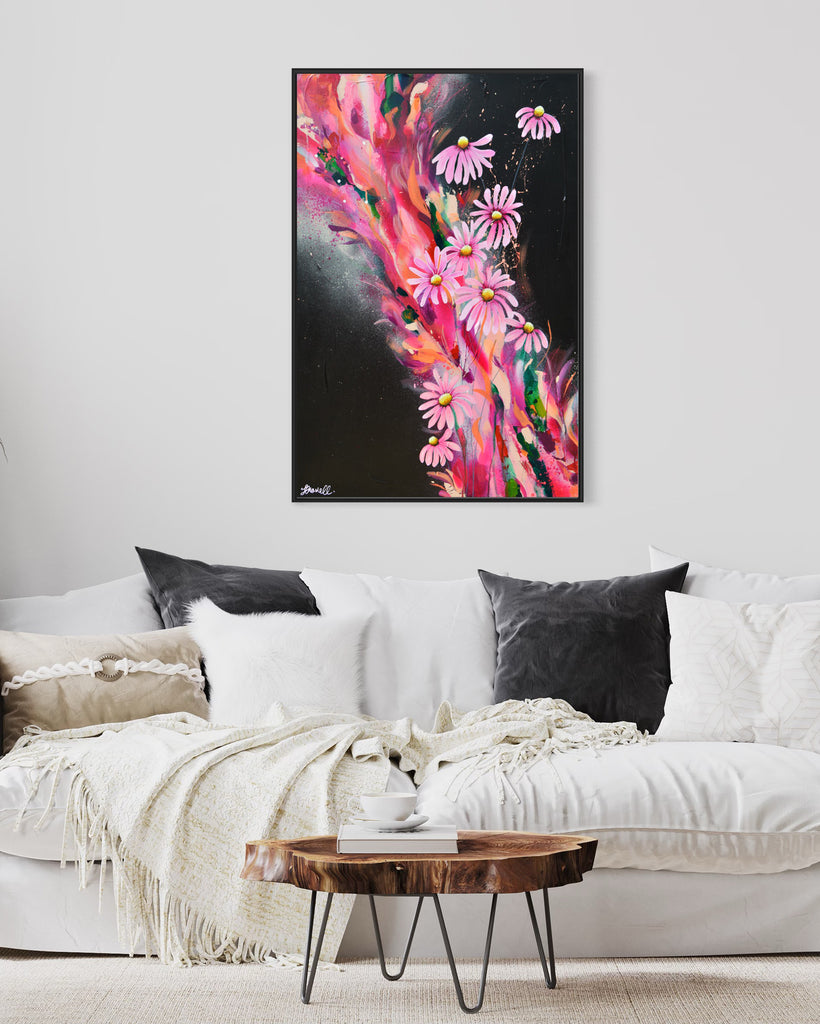 'The Laughter of Daisies' original painting on a cotton canvas by Jasmine Marshall, framed in black/oak. Features pink daises on a colourful abstract details on a black background. Displayed in a neutral living room with white sofa and grey cushions with wooden table.