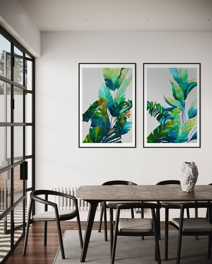 ‘Tropic Duo' Fine Art Print by Jasmine Marshall, framed in black/oak. Premium Giclée print features tropical blue and green leaves on a grey background. Displayed in a kitchen with black dining table and glass doors.