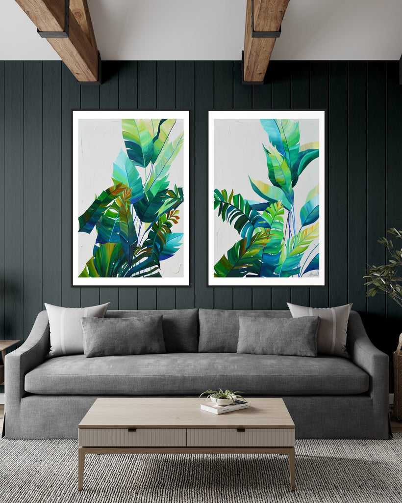 ‘Tropic Duo' Fine Art Print by Jasmine Marshall, framed in black/oak. Premium Giclée print features tropical blue and green leaves on a grey background. Displayed  on a green wall of a living room with wooden ceiling beams, grey sofa, plants and wooden table.