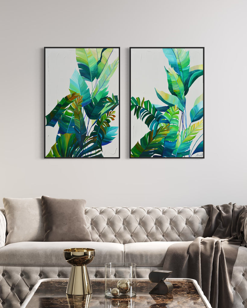 'Tropic Duo' original painting on a cotton canvas by Jasmine Marshall, framed in black/oak. Features tropical blue and green leaves on a grey background. Displayed in a neutral home interior with grey sofas.