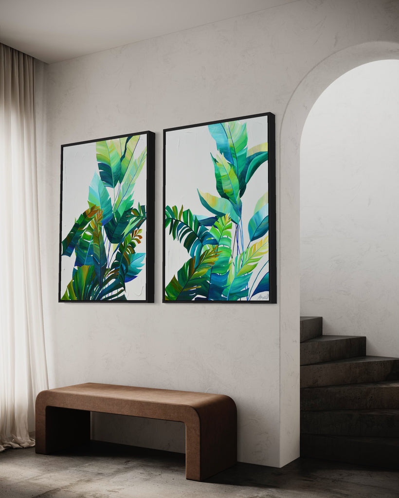 'Tropic Duo' original painting on a cotton canvas by Jasmine Marshall, framed in black/oak. Features tropical blue and green leaves on a grey background. Displayed in a neutral home interior with staircase.