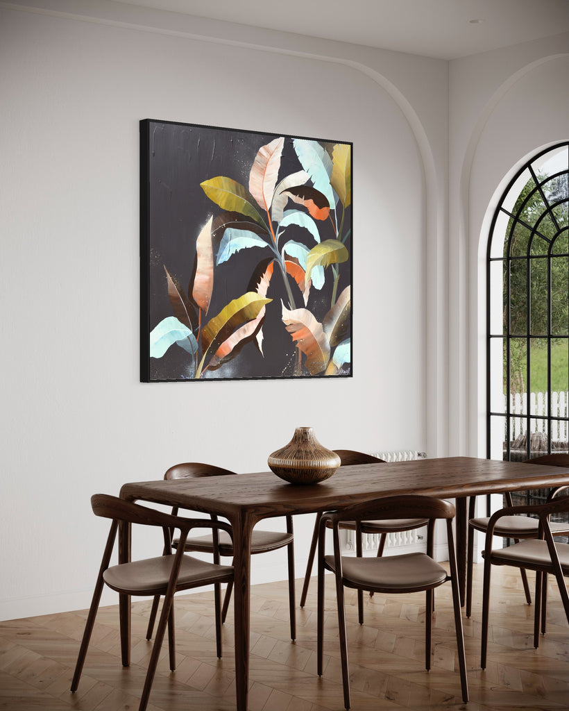 'Under the Canopy' original painting on a cotton canvas by Jasmine Marshall, framed in black/oak. Features a palm tree on a brown background with abstract details. Displayed in a neutral home interior with a brown dining table and glass door.