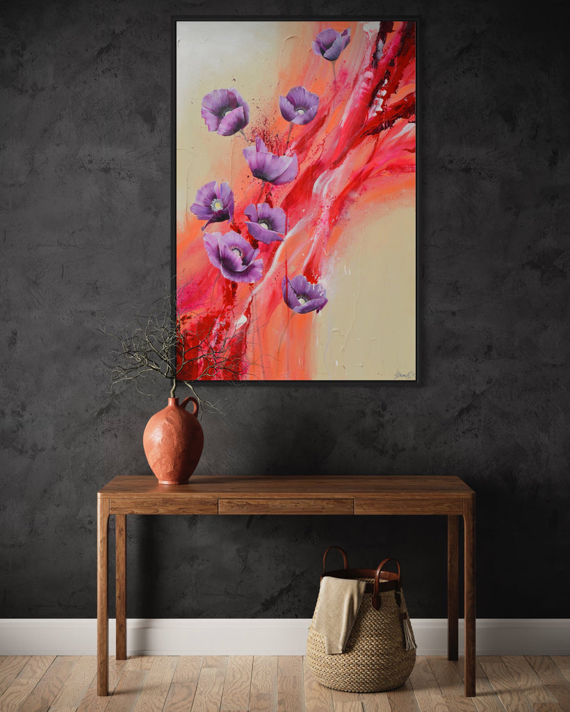 'Making Memories' original painting on a cotton canvas by Jasmine Marshall, framed in black/oak. Features purple poppies on a cream and red abstract background. Displayed on a grey wall with wooden side table..